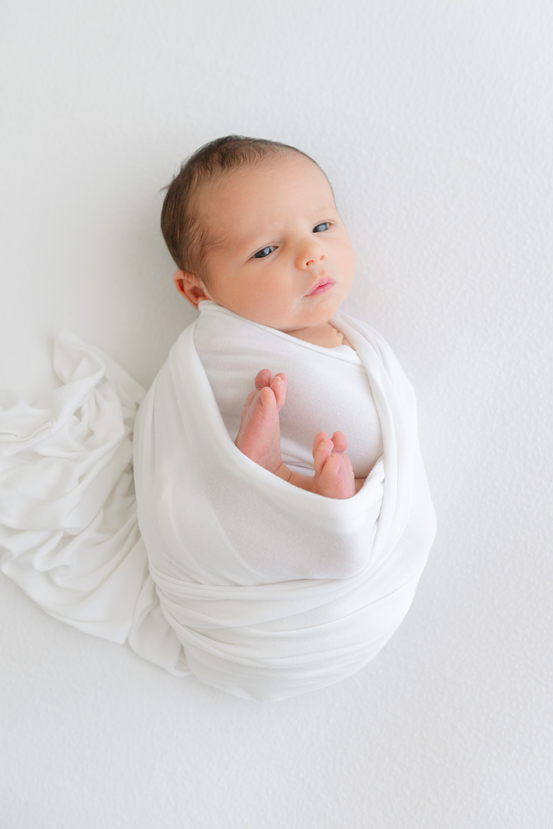 A newborn baby captured by a Shalimar newborn photographer, wrapped in a white swaddle.