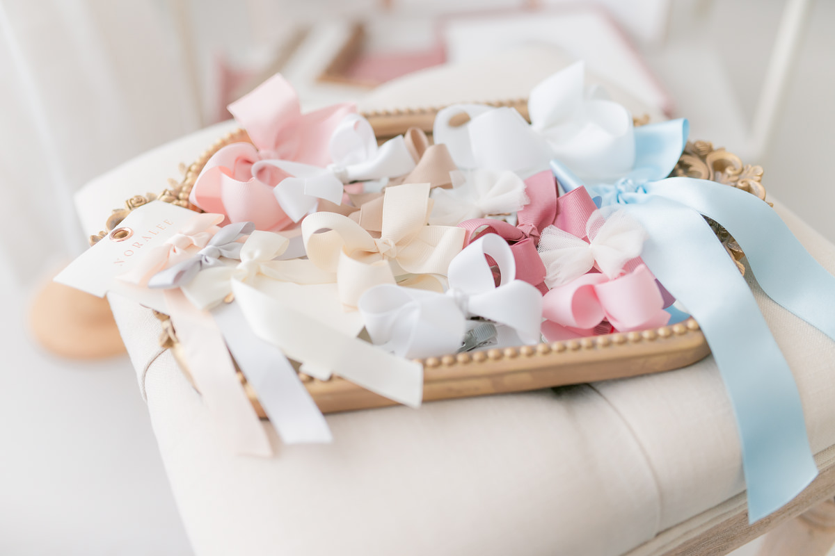 Tray of satin hair bows and ribbons in pink, cream, white and pale blue on a tufted bench