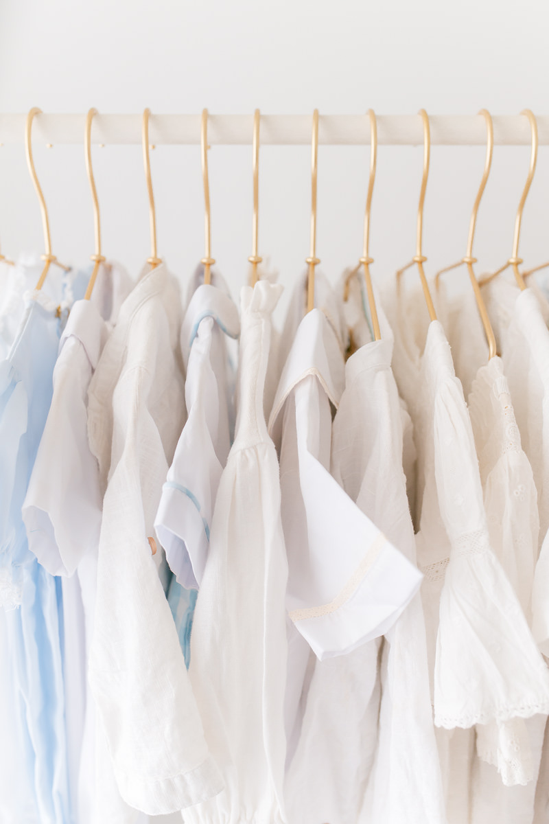 Soft white and pale blue children's outfits on gold hangers for an heirloom portrait session
